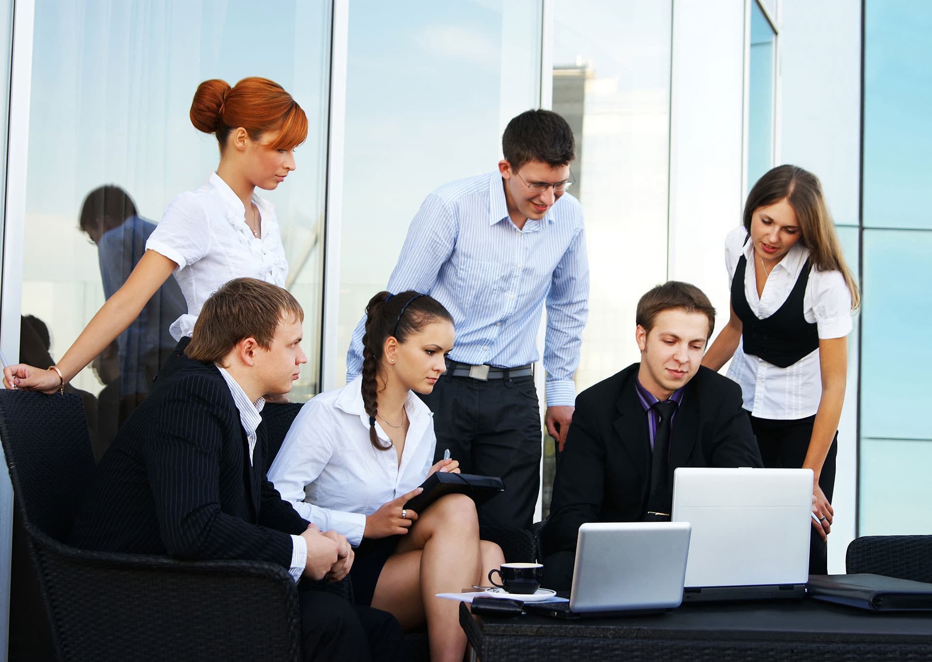 Six young office workers looking at laptop, make work meaningful together